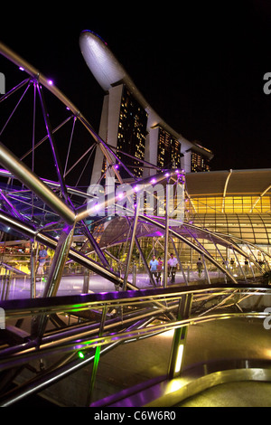 Menschen zu Fuß entlang der modernen Helix-Brücke mit dem Marina Bay Sands Hotel im Hintergrund, die Marina, Singapur Asien Stockfoto