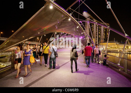 Menschen zu Fuß entlang der modernen Helix-Brücke mit dem Marina Bay Sands Hotel im Hintergrund, die Marina, Singapur Asien Stockfoto