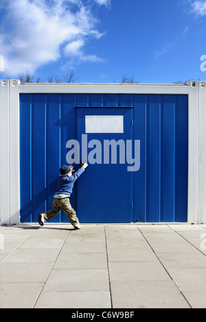 Baby Boy will den Türgriff in der Nähe von blau Mobilfunk Häuser öffnen. Stockfoto