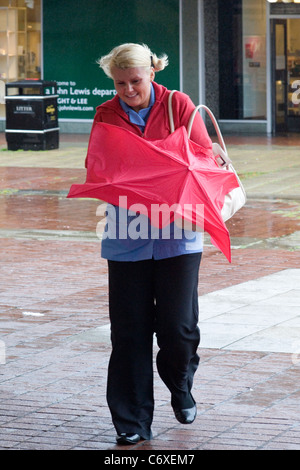 Frau shopping und kämpfen mit einem Regenschirm in den Wind und Regen Stockfoto