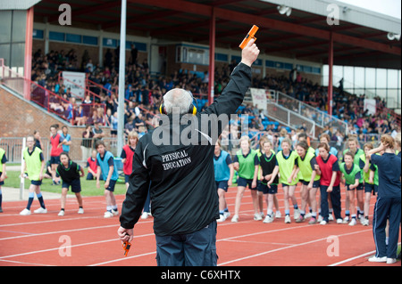 Ein Mann mit Ohrenwärmer feuert ein Startschuss um eine Schule in ein Leichtathletikstadion Rennen zu starten. Stockfoto