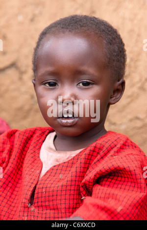 Junge Massai Junge sitzt vor Lehmhütte Stockfoto