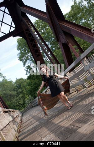 Eine unbeschwerte Brünette Mädchen zu Fuß entlang einer Brücke mit einem Schal im Wind weht. Stockfoto