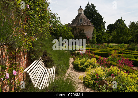 Eine stilvolle Gartenbank fängt der Sommersonne im Parterre des Rousham House in Oxfordshire, England Stockfoto