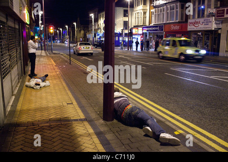 Ein Mann nimmt ein Bild von einer anderen Person auf dem Boden liegend in einer Nacht in Blackpool, England, UK. Stockfoto