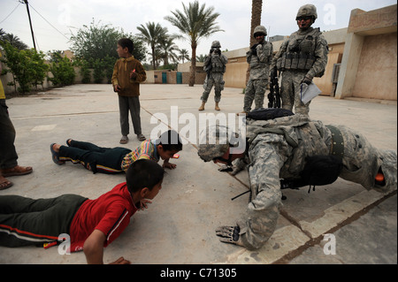 US Army Staff Sgt Josh Hedetniemi macht Liegestütze irakische Kinder außerhalb einer Schule in der Nähe von Sheik Hammad, Irak, am 8. April 2009 unterhalten. Hedetniemi ist von Alpha Company, 1. Bataillon, 111. Infanterie-Regiment, 56. Stryker Brigade Combat Team, 28. Infanterie-Division. DoD-Foto von Sgt. Jacob H. Smith, US-Armee. (Freigegeben) Stockfoto