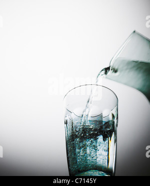 Wasser aus einem Krug in ein Glas gegossen wird. Stockfoto