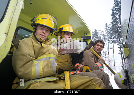 drei Feuerwehrleute mit Achsen sitzen im hinteren Teil ein Feuerwehrauto Stockfoto