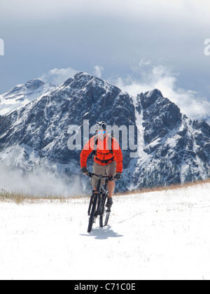 Ein Mountainbiker fährt durch den Schnee am Kronplatz, Felsen im Hintergrund. Stockfoto