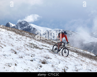 Ein Mountainbiker fährt durch den Schnee am Kronplatz, Berge und Wolken im Hintergrund. Stockfoto