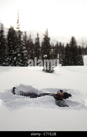 Eine schöne Frauen Lächeln bei der Herstellung eines Schneeengel auf einem unberührten Gebiet bei Sonnenuntergang in Wyoming. Stockfoto