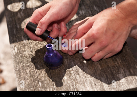 Toe Nail Farben zu ändern. Eine junge Frau malt lila über ihre orange lackierte Fußnägel. Stockfoto
