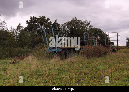 Alten verwilderten Landmaschinen liegend in ein Feld Landschaft Abfälle rostenden gebrochen vergessenen uk England verfallenen Bauernhof-Anhänger Stockfoto