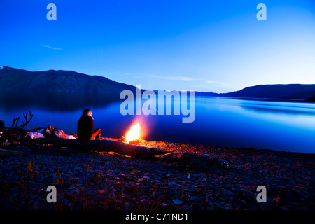 Eine Frau sitzt neben einem schönen Lagerfeuer bei Sonnenuntergang in Idaho. Stockfoto