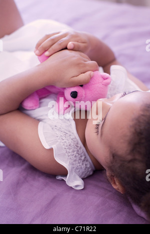 Kleines Mädchen auf Bett liegend mit Teddybär Stockfoto