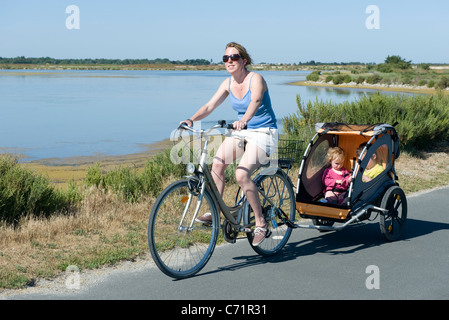 Frau Reiten entlang Radwegs mit Kinder im Fahrradanhänger Stockfoto