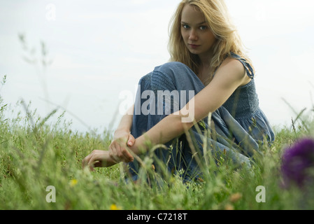 Junge Frau sitzt im Bereich des Grases, Porträt Stockfoto