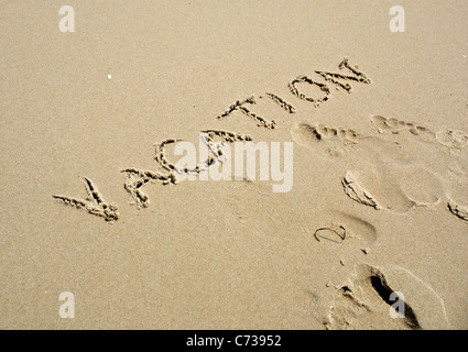 Das Wort Urlaub im Sand zusammen mit einigen Spuren geschrieben. Stockfoto