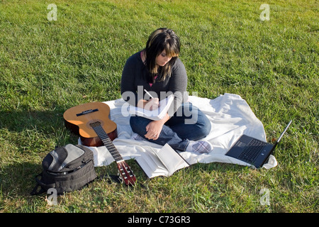 Eine junge Sängerin oder Songschreiber mit ihrer Gitarre und Computer im Freien auf der Wiese. Stockfoto