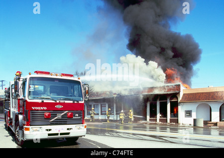 Feuerwehrauto und Feuerwehrleute kämpfen flammendes Feuer in brennende Gebäude mit Wasser, Osoyoos, BC, Britisch-Kolumbien, Kanada Stockfoto