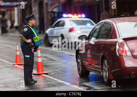 Ein NYPD-Polizisten Bildschirme Autos, wie sie durch eine Sicherheitskontrolle auf der 44th Street zwischen der 7. und 8. Avenue passieren. Stockfoto