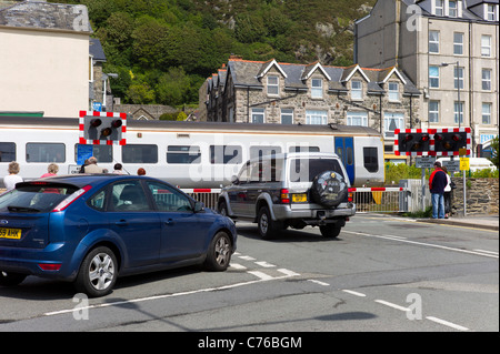 Ein Zug ist ein Bahnübergang Beach Road in der Nähe von dem Stadtzentrum von Barmouth, Nordwales verwenden. Fußgänger und Autos warten auf die Eröffnung. Stockfoto