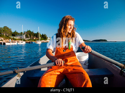 Eine Frau rudert ihr Boot in einem kleinen Hafen bei Sonnenuntergang, nachdem sie Hummer aus Unterwasser fallen vor der Küste gesammelt hat. Stockfoto