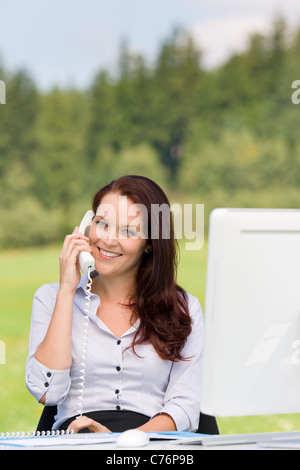 Junge Unternehmerin in der Natur attraktives Lächeln aufrufenden sitzen hinter Tisch Stockfoto