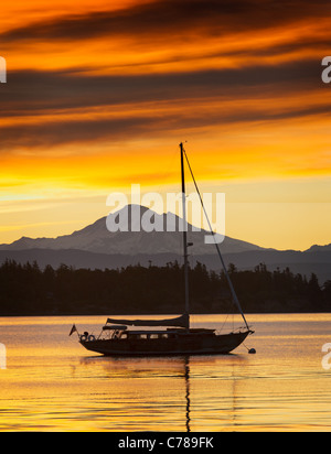 Bei Sonnenaufgang ruht ein Segelboot vor Anker aus Lummi Island, Washington mit Mt. Baker im Hintergrund. Stockfoto