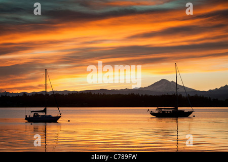 Bei Sonnenaufgang ruht ein Segelboot vor Anker aus Lummi Island, Washington mit Mt. Baker im Hintergrund. Stockfoto