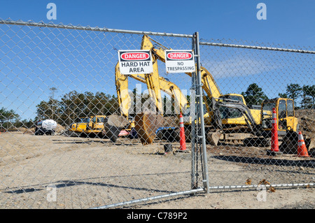 Baustelle mit schwerem Gerät von Metallzaun mit Warnung, Gefahr und Schutzhelm Zeichen umgeben. USA Stockfoto