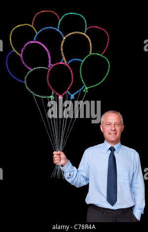 Foto eines ausgereiften Geschäftsmann vor einem schwarzen Hintergrund mit einem großen Haufen Kreide gezeichnet Luftballons Stockfoto