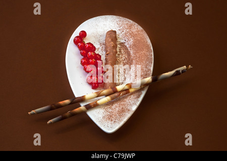 eine lange Schokolade Praline auf einem weißen Teller mit Kakaopulver und rote Johannisbeeren Stockfoto
