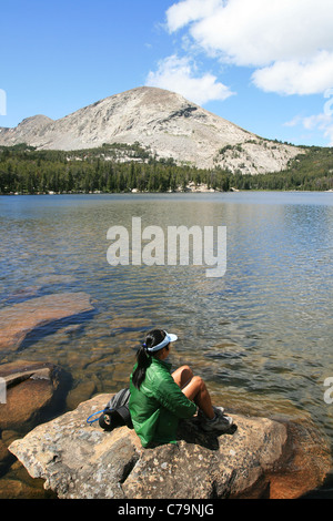 eine Frau in einer grünen Jacke sitzt auf einem Felsen von Silas Alpensee in der Wind River Range, Wyoming Stockfoto