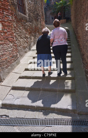 Zu Fuß entfernt, ist eine ältere Frau Stadt Treppe hinauf durch ihre weibliche Helfer in Citta della Pieve, Italien geholfen. Stockfoto