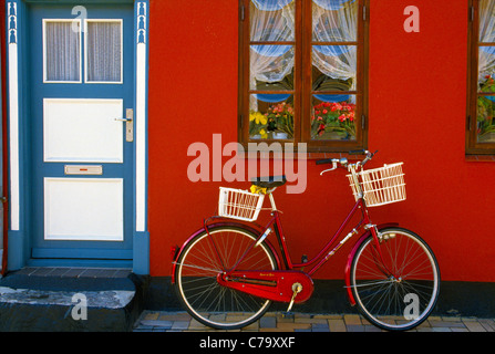 über. Ein rotes Fahrrad vor einer roten Wand geparkt und eine blau-weiße Tür eines Hauses macht eine bunte Straße Tableau in Kerteminde, Dänemark. Stockfoto
