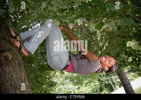 Eine junge Frau hängt spielerisch von einem Ast. Stockfoto