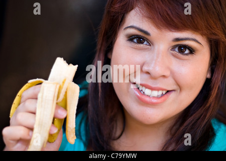 Eine junge Frau, die gerne eine Banane essen. Geringe Schärfentiefe mit stärkeren Fokus auf das Gesicht. Stockfoto