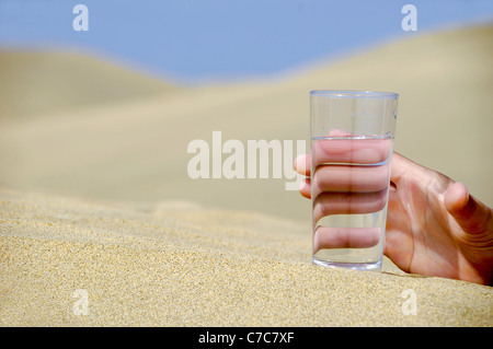 Hand ist bei einem frischen Glas kaltes Wasser in der Wüste erreichen. Stockfoto