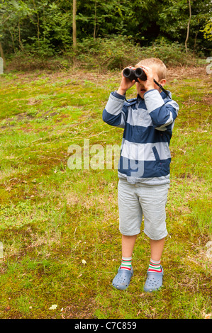 Ein sieben Jahre alter Junge Vogelbeobachtung mit dem Fernglas in Fairhaven Garten Wald und Wasser im Süden Walsham, Norfolk, Großbritannien Stockfoto