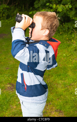 Ein sieben Jahre alter Junge Vogelbeobachtung mit dem Fernglas in Fairhaven Garten Wald und Wasser im Süden Walsham, Norfolk, Großbritannien Stockfoto
