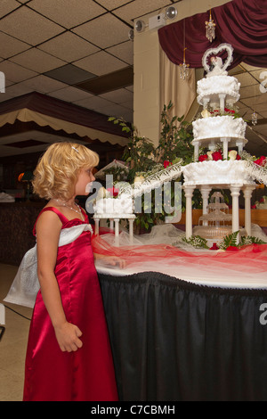 Ein Blumenmädchen, das einen großen, mehrstufigen Kuchen mit beleuchtetem Brunnen unter dem Wasser ansieht und Braut- und Besenfiguren in den USA hochauflösende US-Hochzeiten Stockfoto