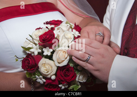 Frisch verheiratete Paare halten Hände und zeigen ihre Eheringe mit weißen und roten Rosen-Blumenstrauß horizontal in den USA Hi-res Stockfoto