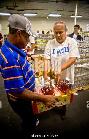 Eine freiwillige Hispanic Frau verleiht ein afrikanischer amerikanischer Mann an eine Wohltätigkeitsorganisation Lebensmittelvertrieb in Santa Ana, CA. Hinweis T-shirt Essen. Stockfoto