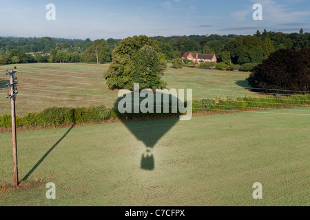 Schatten der Heißluftballon auf Feld vor Stromleitungen, England Stockfoto