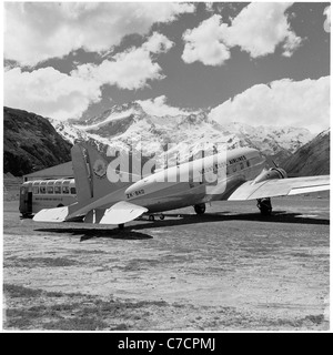 Neuseeland, 1960er Jahre. Mount Cook Flugzeug sitzt auf einem grasbewachsenen Hang Start-und Landebahn von Bergen umgeben. Stockfoto