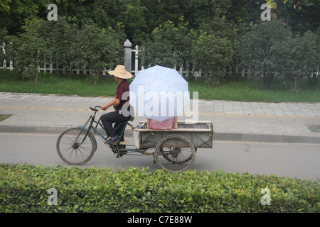 Ein Mann mit einem Dreirad-Wagen mit einer Frau mit einem Sonnenschirm in Jingzhou, China Stockfoto