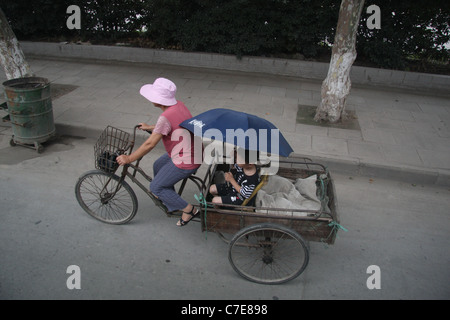 Eine Frau mit einem Dreirad-Wagen tragen einen kleinen Jungen mit einem Sonnenschirm in Jingzhou, China Stockfoto