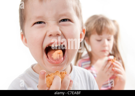 Kinder essen einen Kuchen. Junge Grimassen und streckt die Zunge Stockfoto