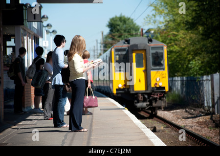 Passagiere warten auf einem Bahnsteig Bahnhof wie ein Zug nähert. Stockfoto